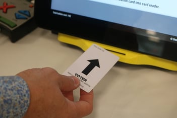 A hand is shown putting a voter card into a Georgia voting machine