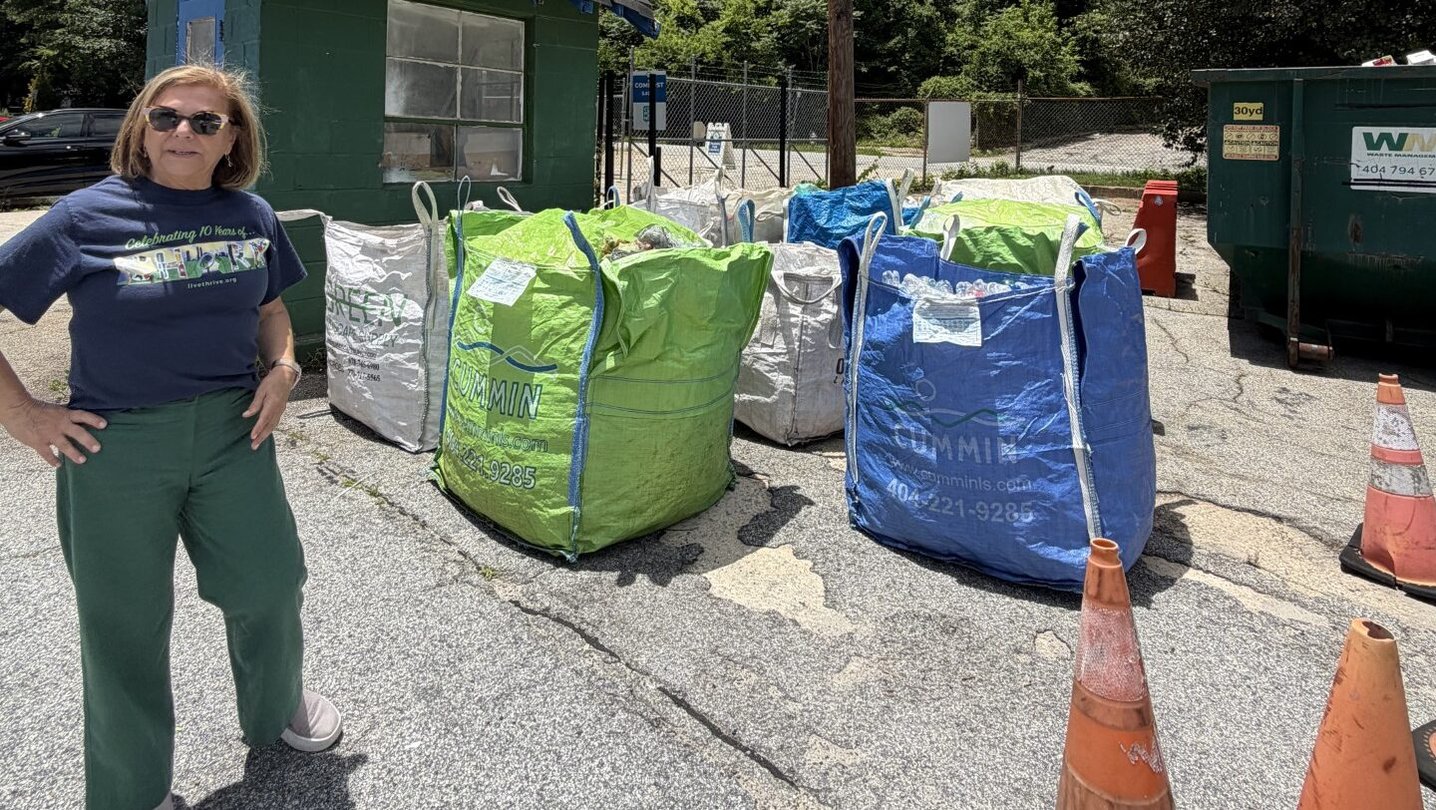 Live Thrive founder Peggy Whitlow Ratcliffe stands to the left of blue and bag large bags of baled recyclables. There's two orange traffic cones on the right in the foreground of the photo.