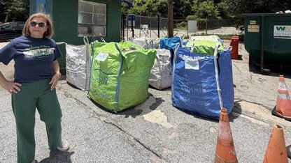Live Thrive founder Peggy Whitlow Ratcliffe stands to the left of blue and bag large bags of baled recyclables. There's two orange traffic cones on the right in the foreground of the photo.