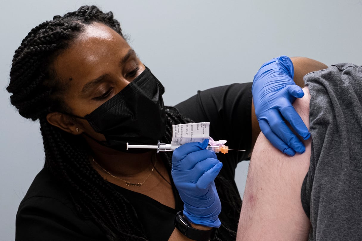 A person in scrubs holds as a needle as they are about to give another person a shot in the arm
