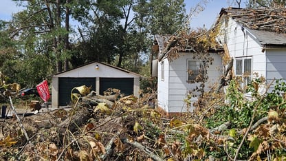 Broken tree limbs cover a yard and the top of a house and two-car garage after a major storm