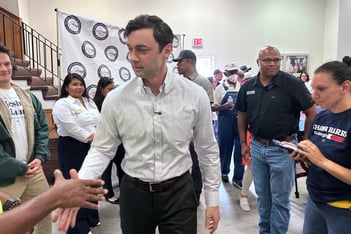 Senator jon ossoff in a white button down shirt shakes hands with people in a crowded room