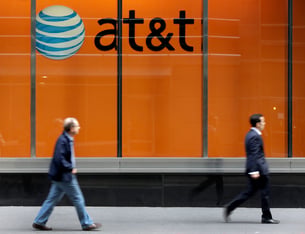 Two people walk in front of an orange ATT display in New York.