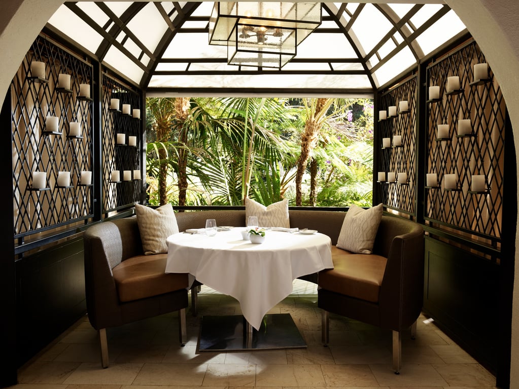 This Culinary Gem Tucked Within Bel-Air’s Landmark Hollywood Glamour Hotel Is LA Dining at Its Best | The Restaurant at Hotel Bel-Air entrance | The Restaurant at Hotel Bel-Air dining room | The Restaurant at Hotel Bel-Air outdoor seating | The Restaurant at Hotel Bel-Air salmon dish | The Restaurant at Hotel Bel-Air dinner spread | The Restaurant at Hotel Bel-Air table with people | The Restaurant at Hotel Bel-Air fireplace | The Restaurant at Hotel Bel-Air covered seating