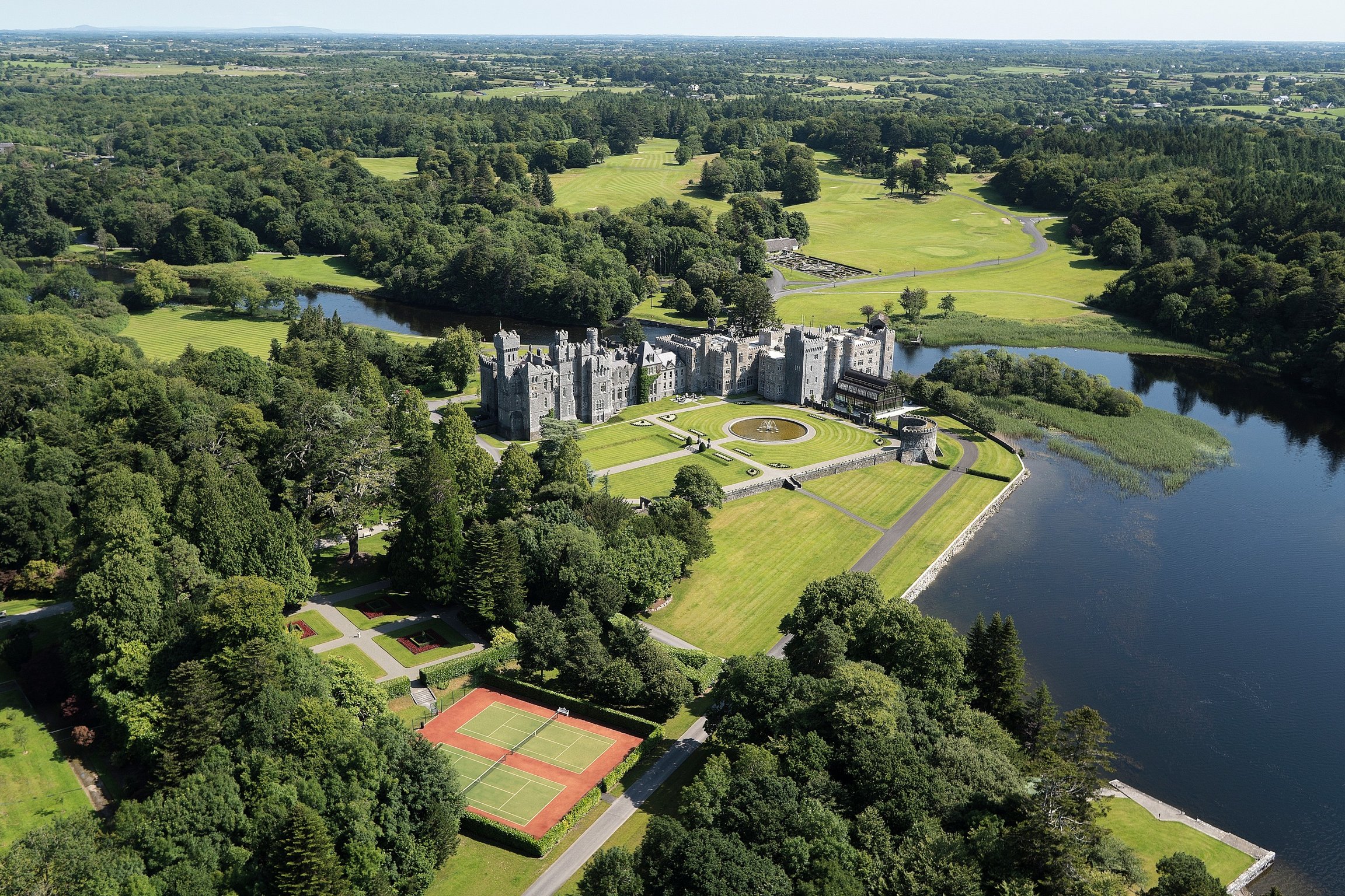 Experience Regal Living in This Private Irish Castle Retreat | Ashford Castle aerial view | Ashford Castle bedroom suite | Ashford Castle restaurant seating | Ashford Castle bathroom tub | Ashford Castle dining room