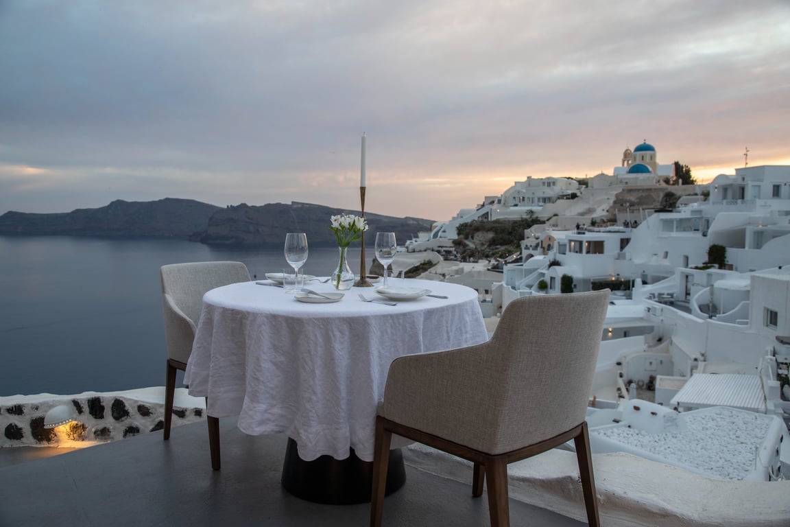 Indulge in Authentic Greek Flavors with Breathtaking Caldera Views in Oia, Santorini | MIA's Santorini balcony table | MIA's Santorini restaurant seating | MIA's Santorini seating with ocean view | MIA's Santorini appetizer | MIA's Santorini signature dinner | MIA's Santorini signature desert | MIA's Santorini indoor dining | MIA's Santorini tablecloth