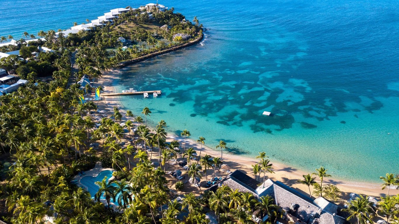 This Iconic Antigua Resort Is a World-Class Caribbean Getaway | Curtain Bluff aerial view | Curtain Bluff balcony overlooking the beach | Curtain Bluff private beach | Curtain Bluff bedroom suite | Curtain Bluff sunset | Curtain Bluff beachside view