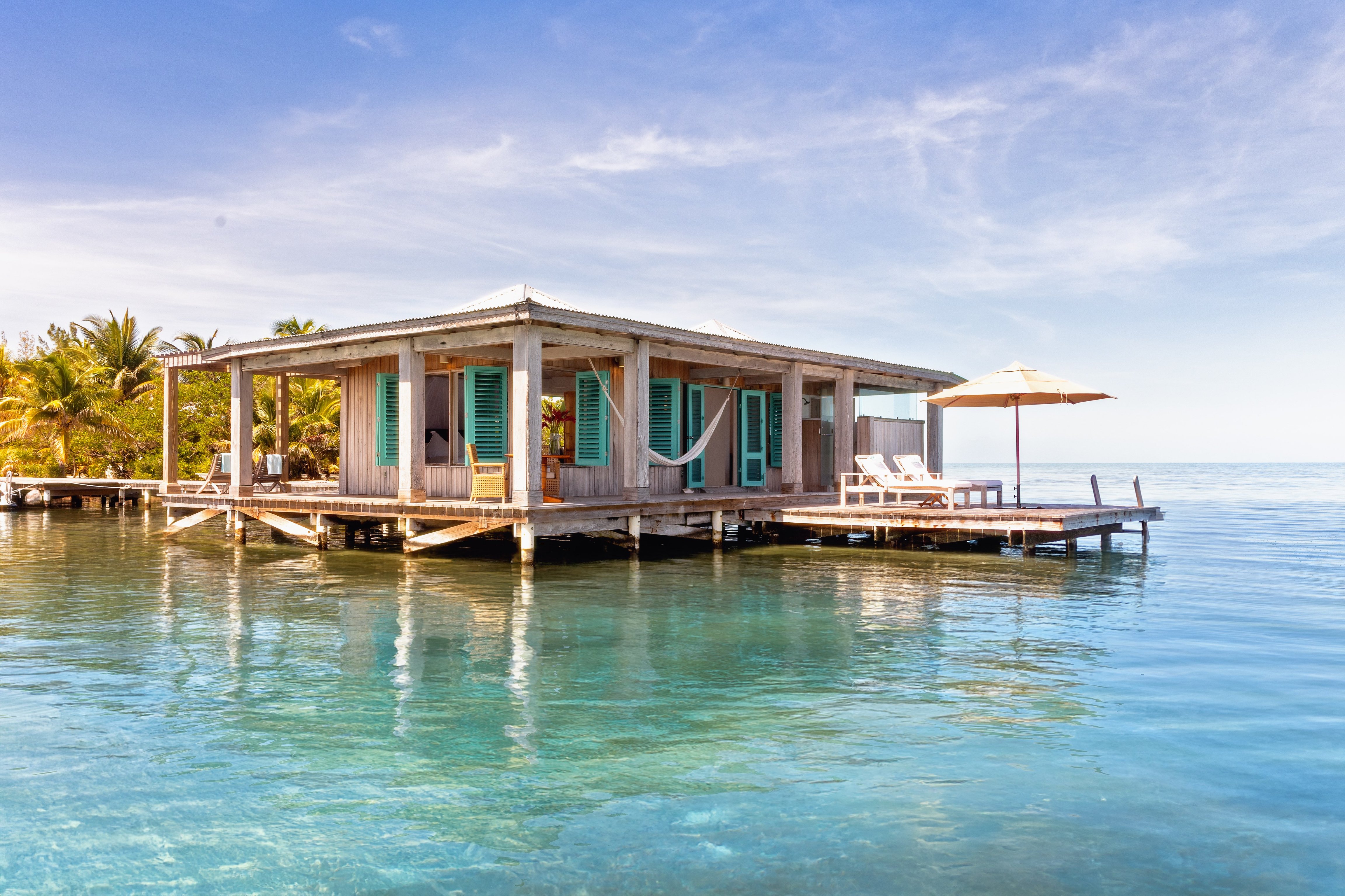 Overwater bungalow with turquoise shutters and private deck at Cayo Espanto, Belize.