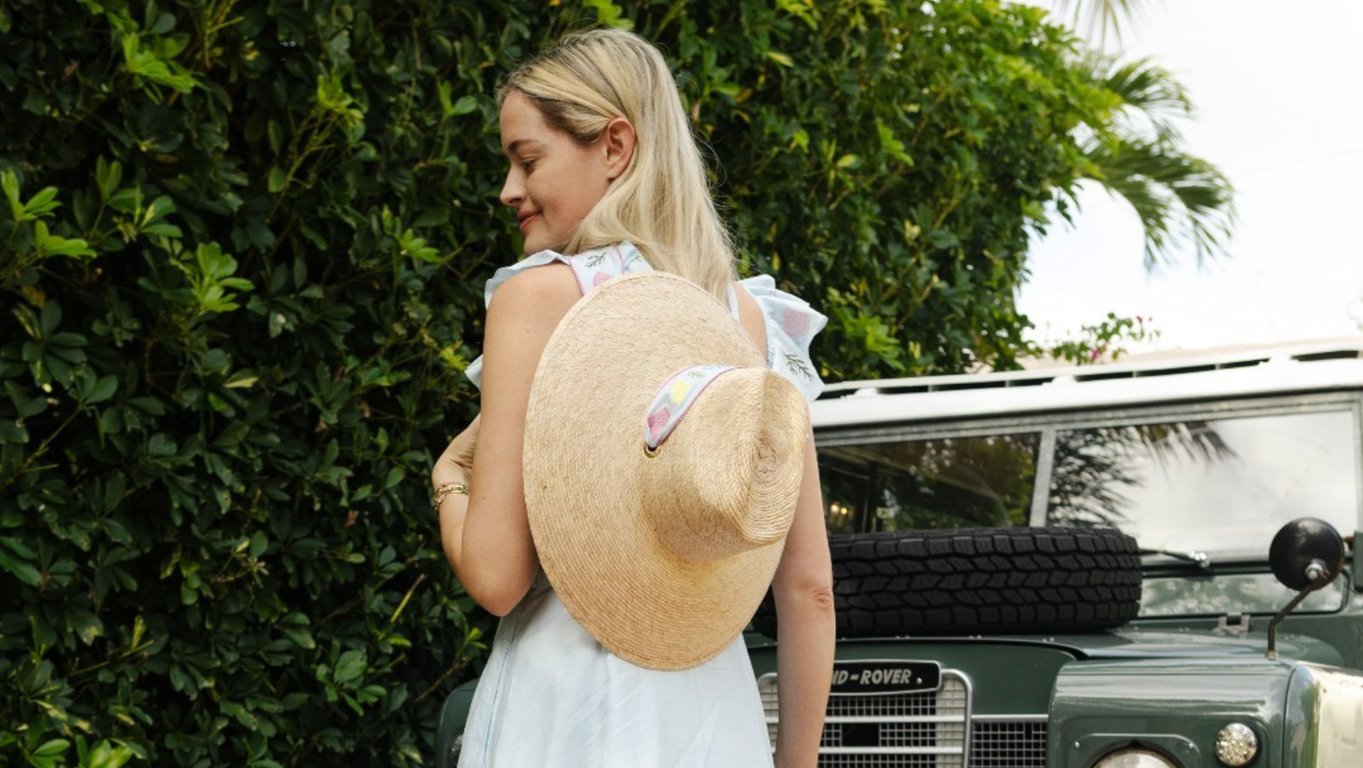 Rosewood Bermuda Partners with Sarah Bray Bermuda on Luxury Sustainable Sun Hats and Eco-Friendly Initiatives for World Ocean Day and Beyond | Sarah Bray Bermuda against green shutters | Sarah Bray Bermuda face covered by straw hat | Sarah Bray Bermuda straw hat by water | Sarah Bray Bermuda focused on straw hat | Sarah Bray Bermuda scarf | Sarah Bray Bermuda with straw hat
