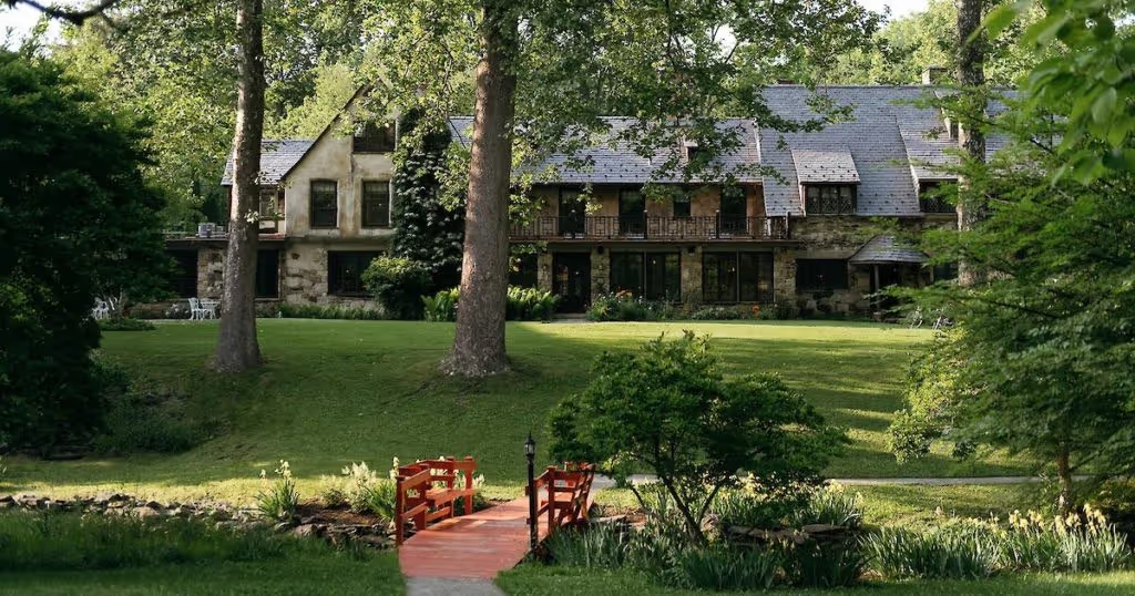 This Historic Hudson Valley Hotel is an Ideal Year-Round Escape for Creatives | Troutbeck Hotel exterior view | Troutbeck Hotel outdoor pool | Troutbeck The Manor House suite | Troutbeck suite bedroom | Troutbeck restaurant dining | Troutbeck The Dining Room restaurant | Troutbeck Hotel The Barns Wellness Center | Troutbeck Hotel Sauna