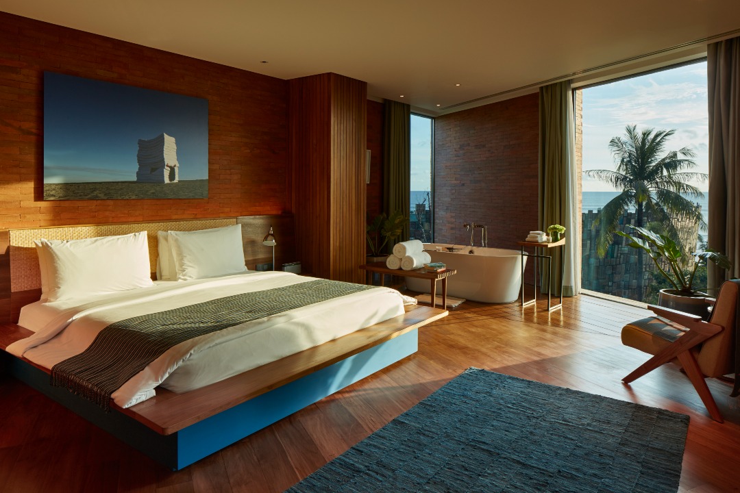 This Beachfront Hotel in Bali Is One Of The Most Unique Eco-Friendly Resorts | Potato Head Studios entrance | Potato Head Studios poolside cabanas | Potato Head Studios bedroom suite and tub | Potato Head Studios green seating area | Potato Head Studios wooden room with bottles along the wall | Potato Head Studios wall art