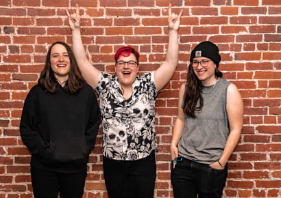three people in Random Ideas band standing by a brick wall and smiling
