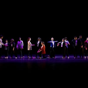 A group of dancers performing on stage under dim lighting, showcasing synchronized movements in colorful outfits.