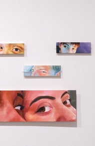 An art exhibit featuring close-up portraits on the wall with a person observing the artwork nearby.