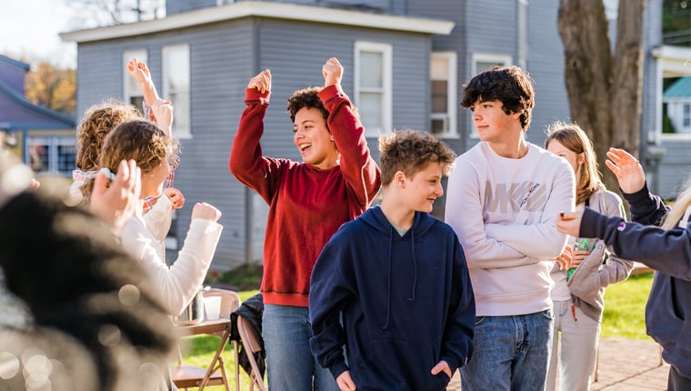 Group of young people outdoors celebrating with some raising their hands in front of a house on a sunny day