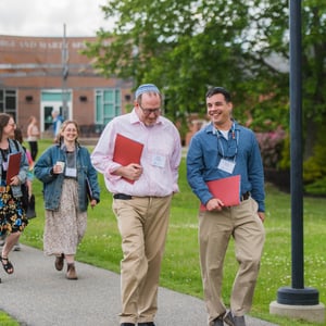 Group of people walking outdoors in a parklike setting holding folders and engaging in conversation Bright day greenery around
