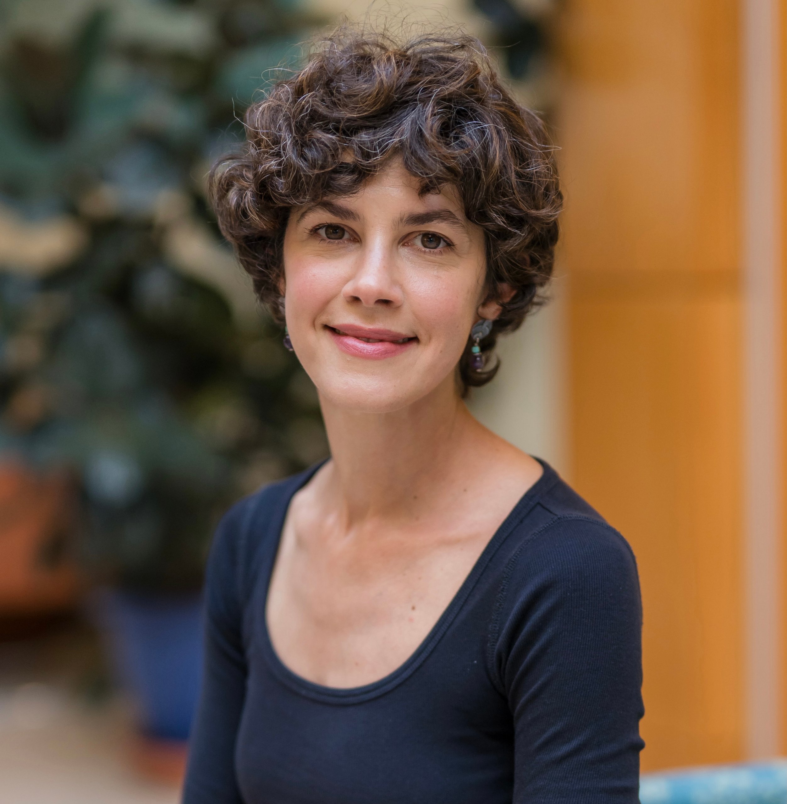 Portrait of a woman with short curly hair wearing a black shirt smiling softly in a serene indoor setting
