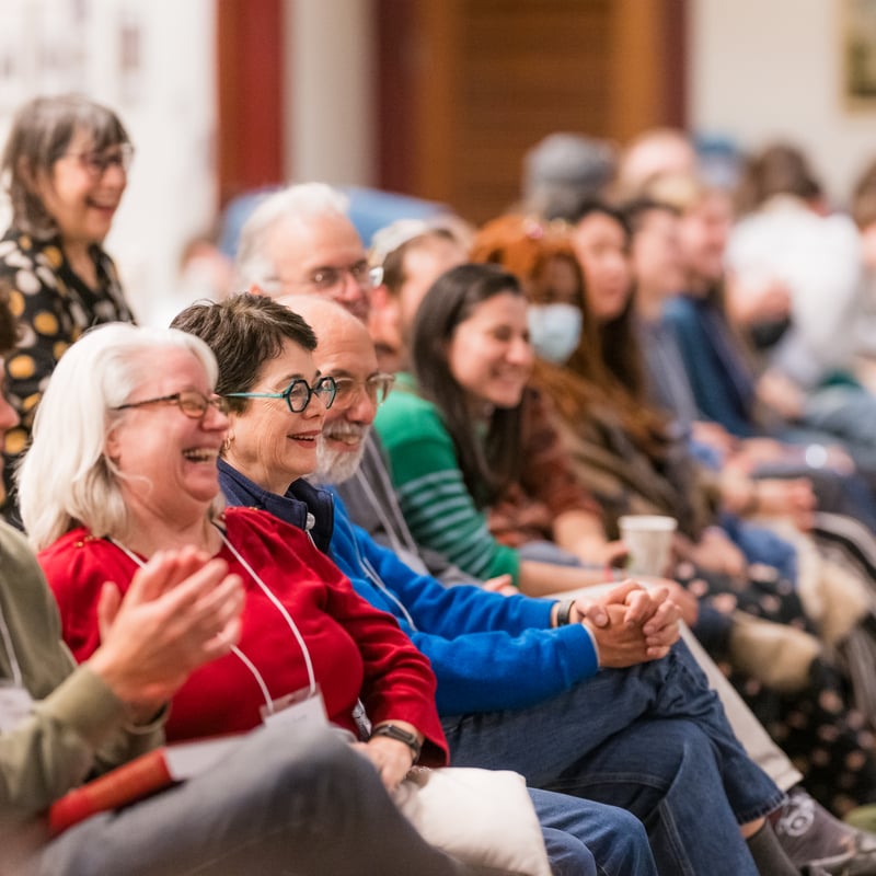 A group of people sitting together smiling and engaging in a lively discussion at a gathering or event
