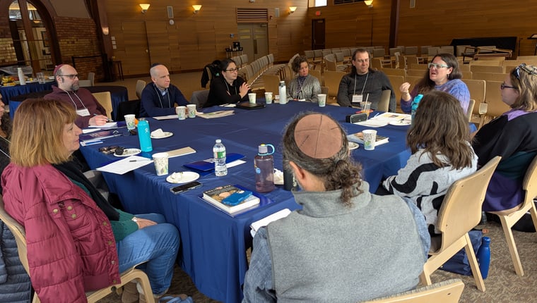 Group of people seated around a table engaged in discussion at a workshop or meeting in a warm inviting space