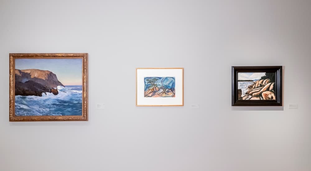 Three framed landscapes, each depicting rocky terrain, hung in a gallery.