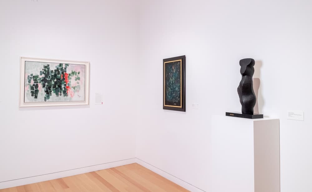 Two abstract, framed paintings and one sculpture on a plinth in a gallery.