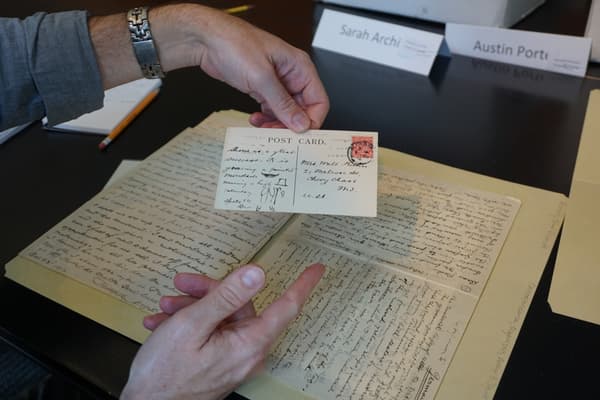 Person holding a vintage postcard over a handwritten letter on a table.
