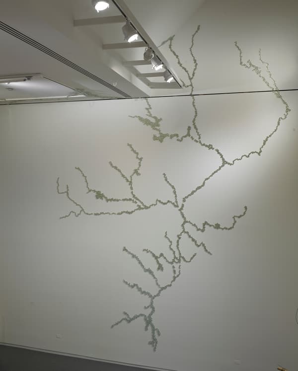 Installation of an artwork made of glass marbles affixed to a white wall.