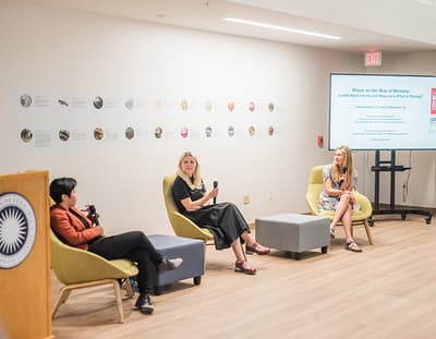A group are seated in yellow chairs in a semi circle, holding up mircophones.