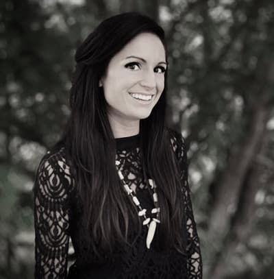 Black and white portrait of a person in a lace dress with a statement necklace, set against a blurred background of foliage.