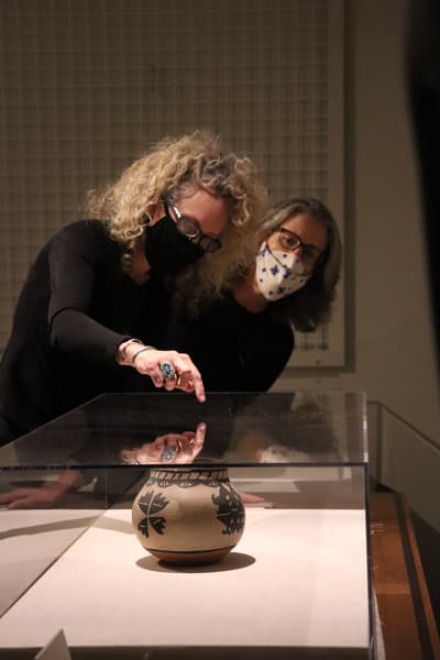 Two researching look at a vessel in a glass vitrine, one person pointing at it.