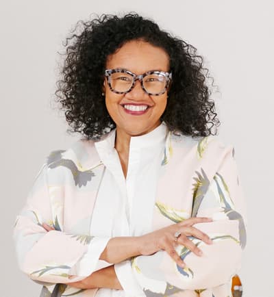 Person wearing glasses and a patterned blazer, smiling and crossing their arms.