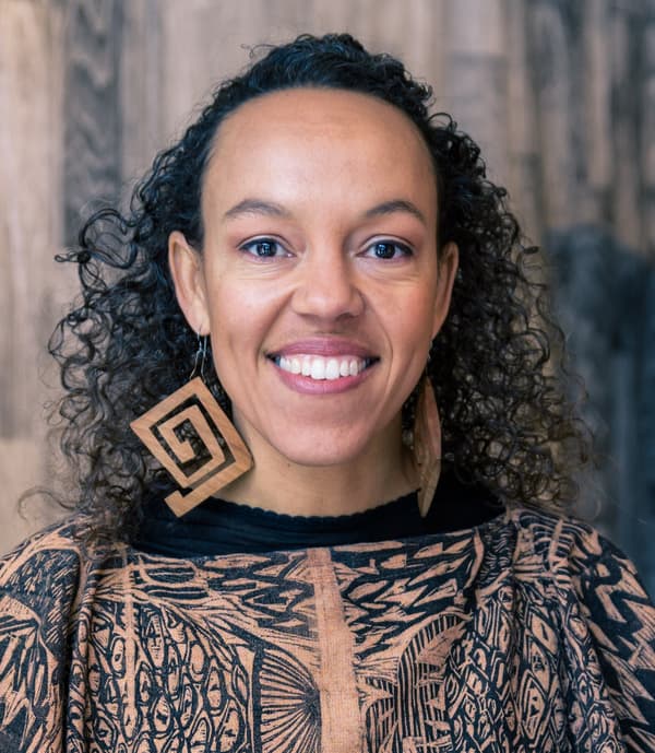 Paula Wilson faces the camera, smiling, and wearing large geometric earrings.