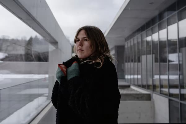 A woman standing outside near concrete an glass architecture wrapping a coat around herself.