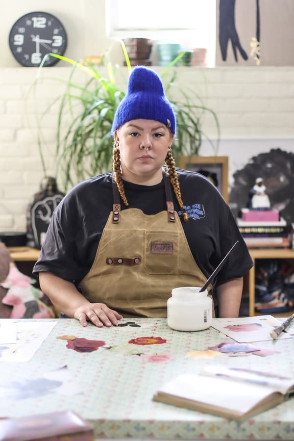 Genevieve Gaignard faces the camera, unsmiling, wearing a blue beanie and beige overalls.