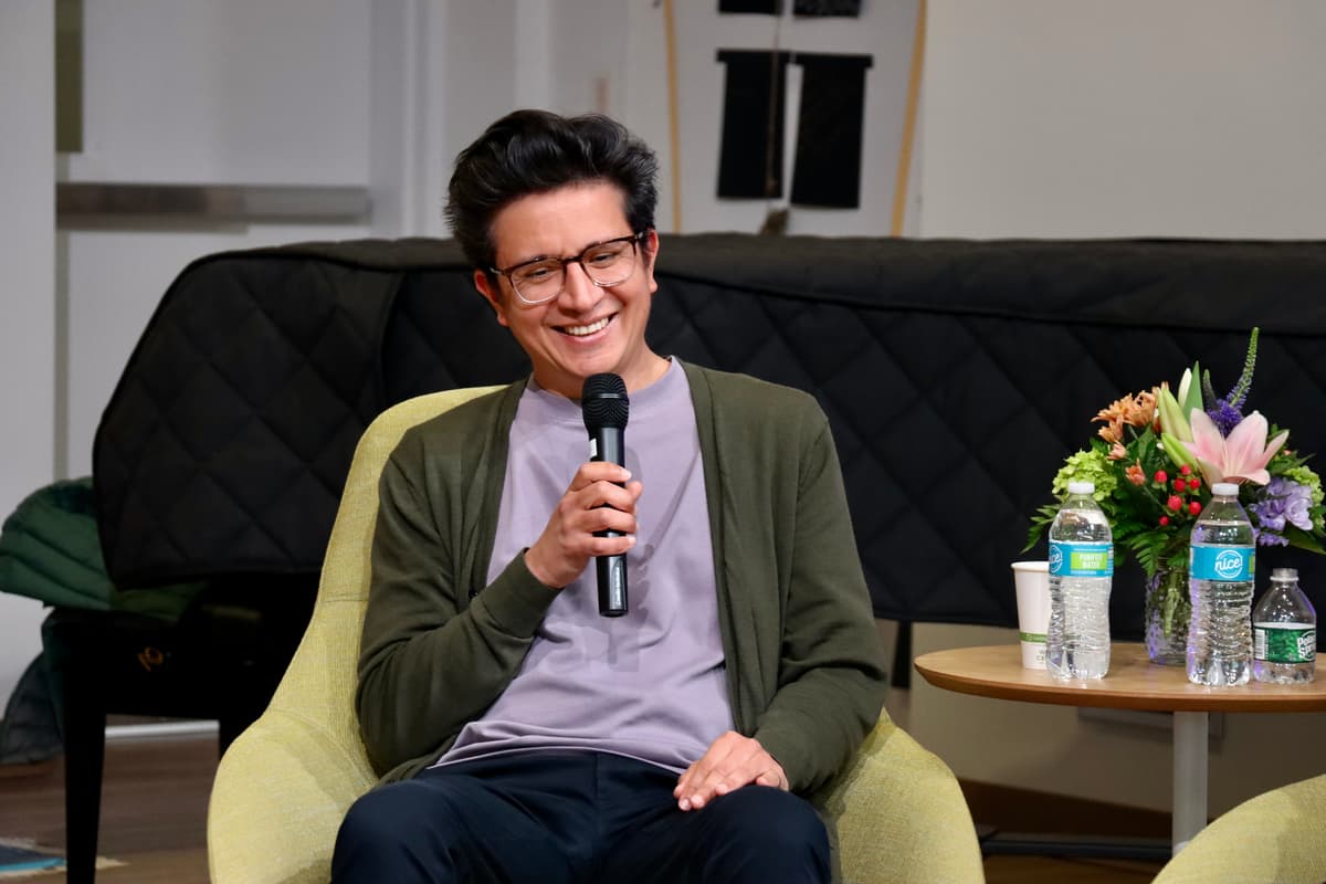 Oscar Santillán holds a microphone up and smiles while seated in a green chair.