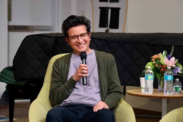 Oscar Santillán holds a microphone up and smiles while seated in a green chair.