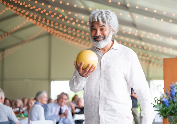 Conceptual artist Fred Wilson smiles at the camera after receiving the 2023 Cummings Award for Artistic Excellence, holding the award up to the camera.