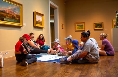 Colby museum staff reading book to group of young learners and caregivers in museum galleries