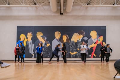 Students performing in front of painting by Alex Katz