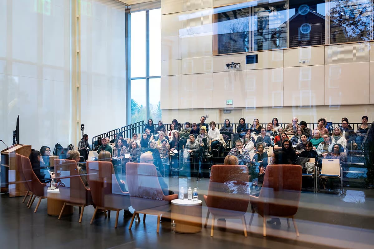 A group of people convening for a discussion about the state of American Art in a high-ceilinged auditorium with glass windows
