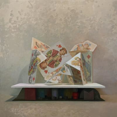 Playing cards folded in a way that allows them to balance against one another on top of a white surface supported by multiple colorful shapes.