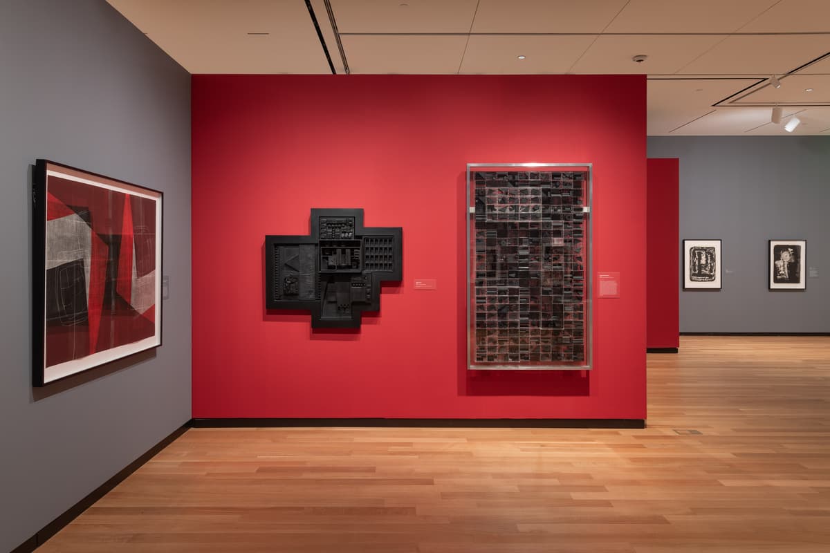 Museum gallery with red and grey walls with mixed media hanging works of art.