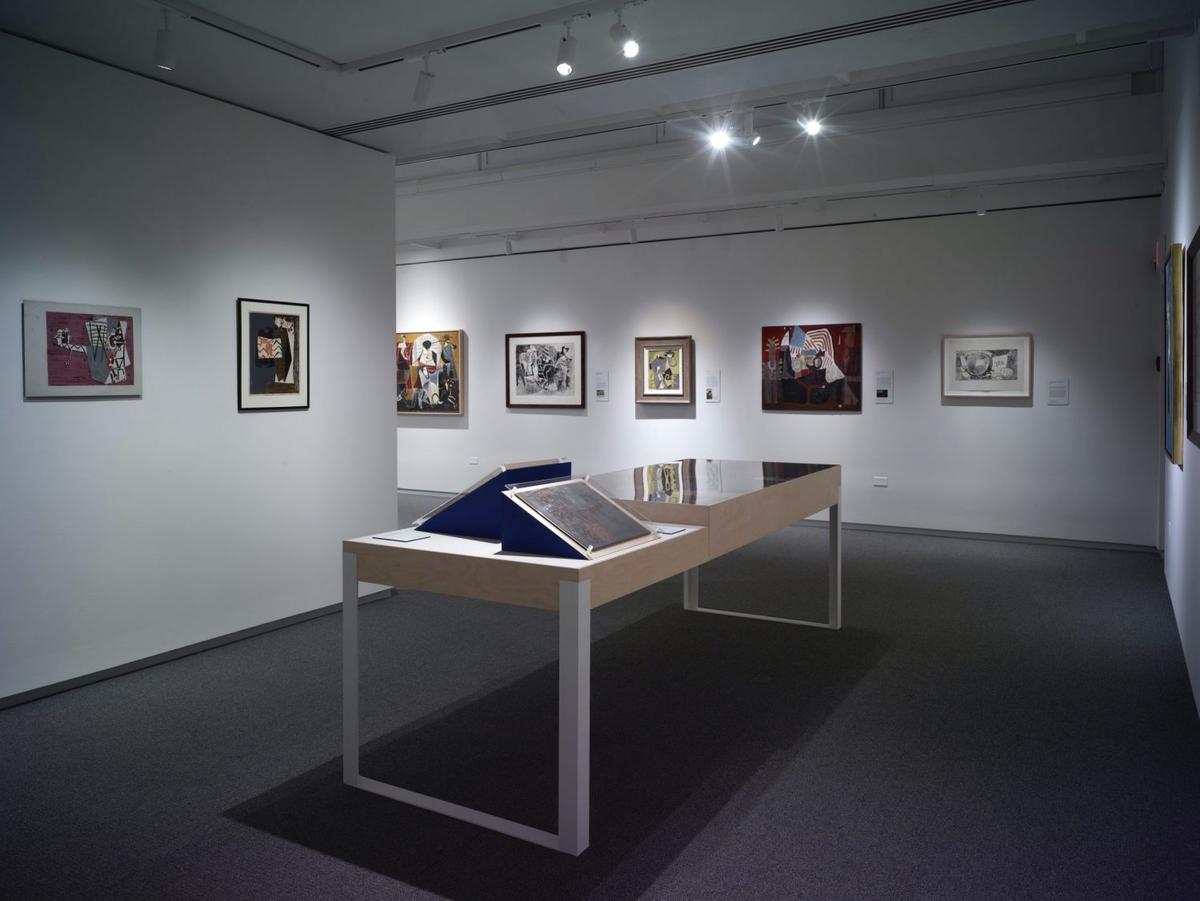 Art gallery interior with abstract and contemporary paintings on white walls with a plexiglass case in the center.