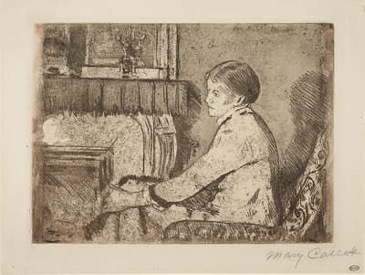 A young woman seated in a large arm chair in front of a fireplace. She rests her arms on top of her knees.