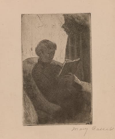 A seated woman reading a book in a large arm chair.