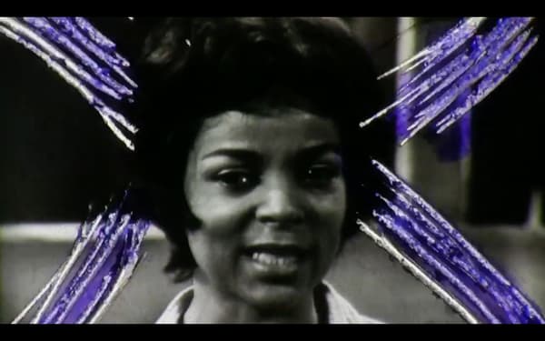A video still of a woman with white and purple markings around her.