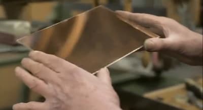 Hands holding a reflective metal sheet in a workshop.