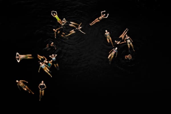 Video installation with a number of people swimming with a black background.