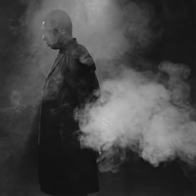 A figure in a trench coat emerging from a cloud.