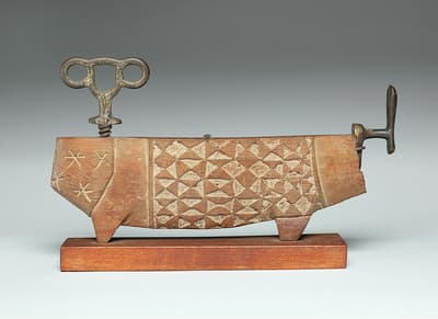 A carved wooden object resembling an abstract animal with geometric patterns and metal wind-up mechanisms.